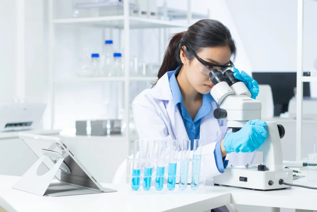 Uma cientista de jaleco branco e luvas manuseia um líquido com uma pipeta em um laboratório, representando a pesquisa sobre o aumento dos casos de infertilidade.