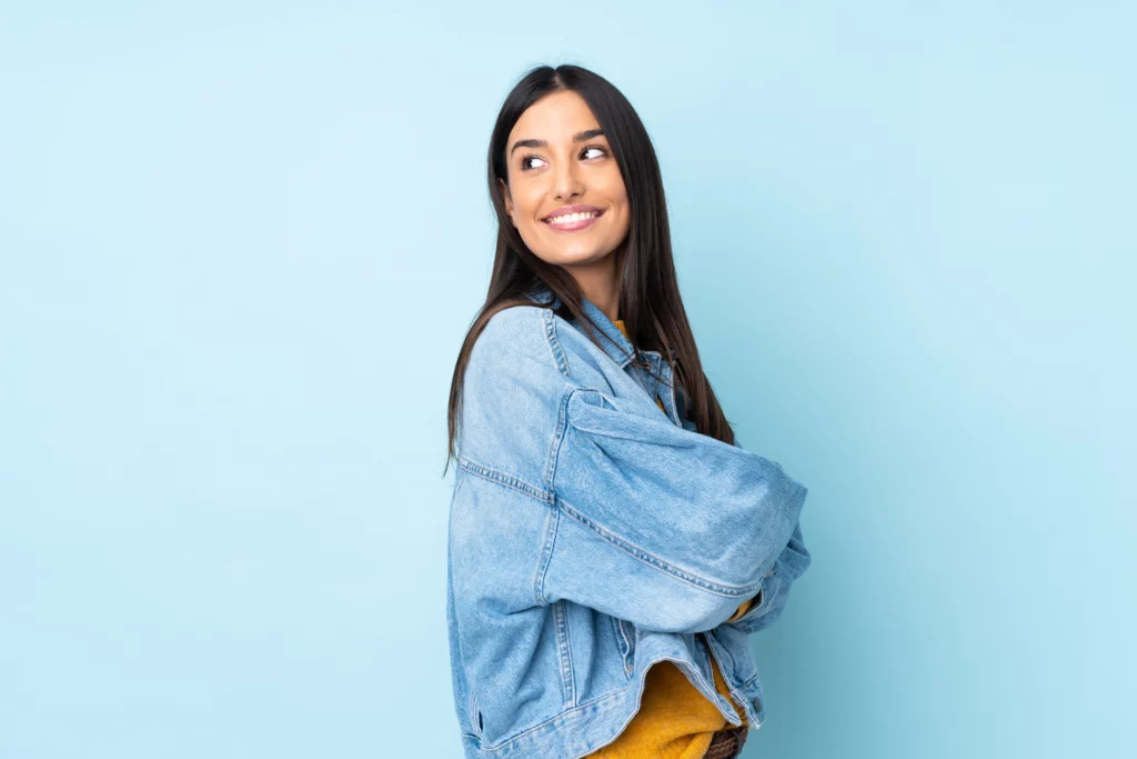 Pessoa de cabelo longo e liso, vestindo jaqueta jeans, em frente a um fundo azul-claro, indicando uma mulher em idade para congelar os óvulos