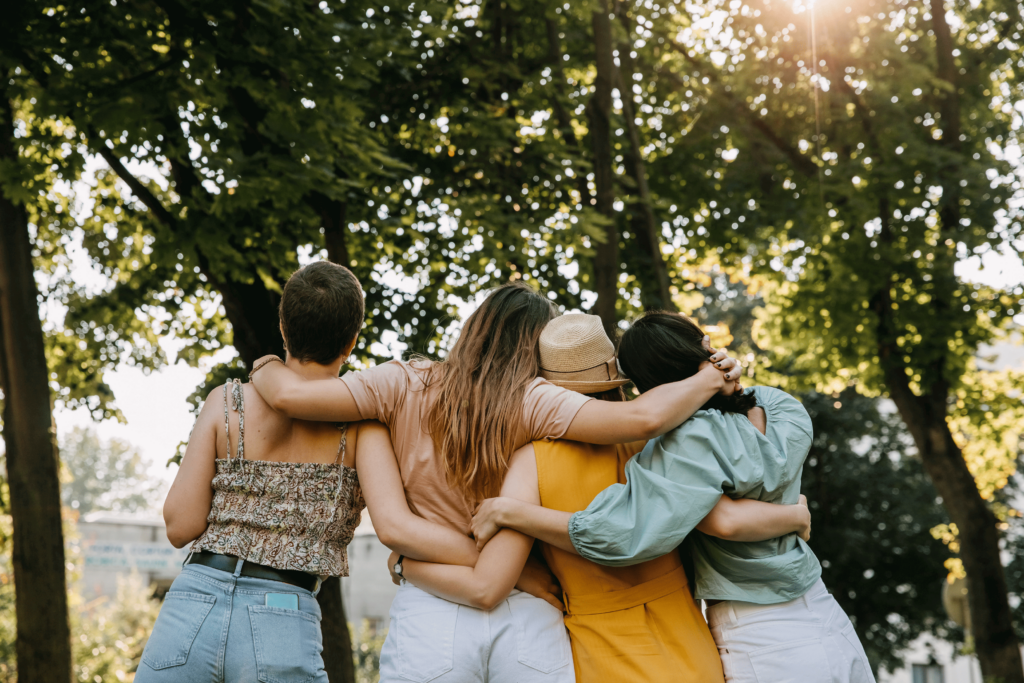 Grupo de quatro mulheres de costas para a câmera, se abraçando. Elas estão reunidas em frente a árvores. A imagem representa as mulheres citadas nos depoimentos sobre congelamento de óvulos.