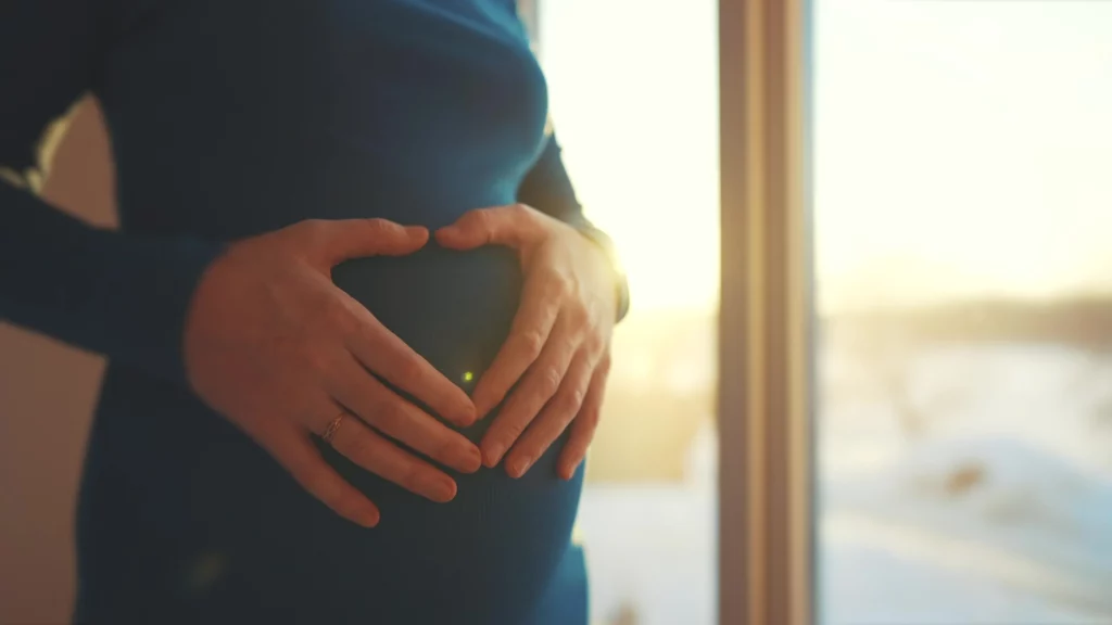 Mulher grávida fazendo um formato de coração com as mãos na barriga, representando a gravidez aos 20, 30 e 40 anos.