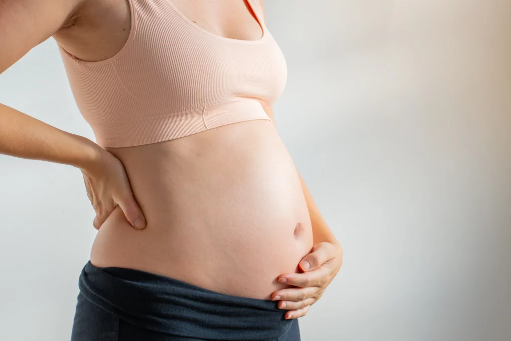 Close-up da barriga de uma mulher grávida, com uma mão apoiando as costas, representando a experiência da gravidez após laqueadura ou outras circunstâncias.